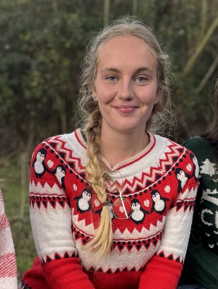 Katie sites outdoors wearing a Christmas jumper smiling to camera