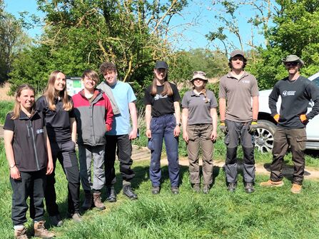 8 people in outdoor workwear stand in a sunny nature reserve
