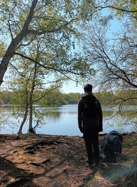 Teen boy stands looking out over lake in shade of trees