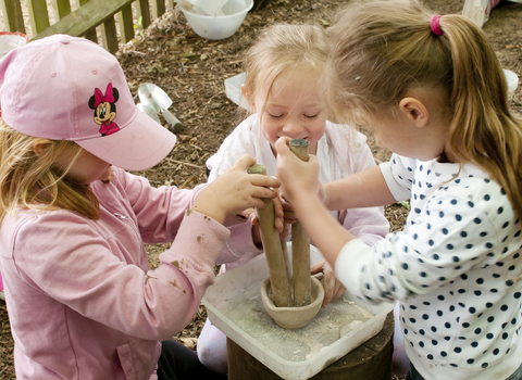 Three children with long fair hair crushing chalk in a bowl using sticks