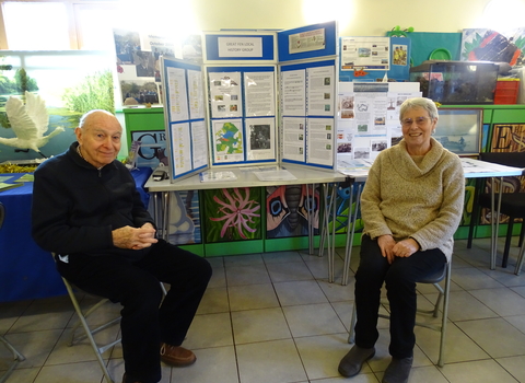 Alan Malt and Sue Knight sit either side of a table with a tri-fold display board atop it showing Great Fen heritage information