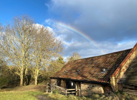 a rainbow is shining in blue sky over a brick building with tiled roof