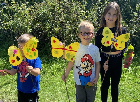 Three children holding paper butterflies on sticks