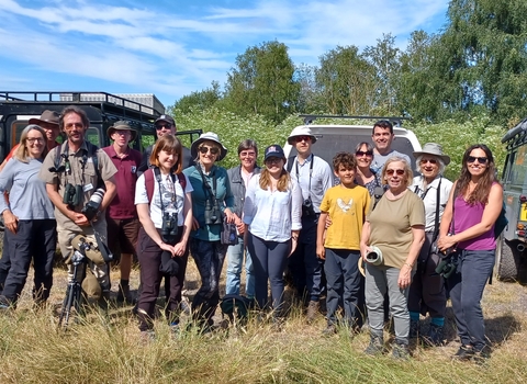 Group of adults standing in sunshine in front of three 4x4 vehicles in a nature reserve