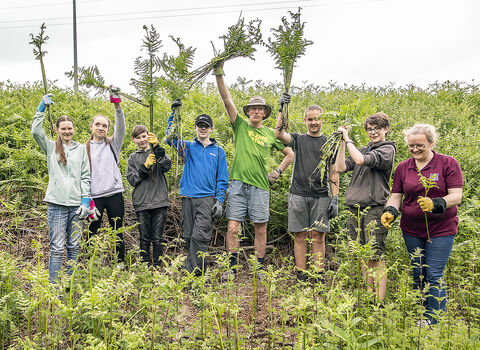Young people and staff hold plants they've been cutting over their heads
