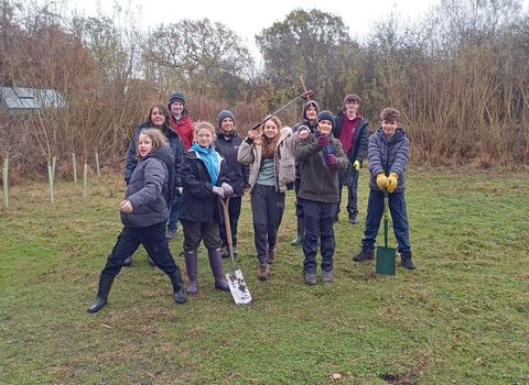 8 young people stand with two staff members, all wearing winter coats, boots, gloves and a few holding gardening tools